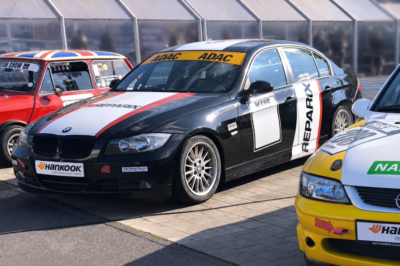 Schwarzer BMW 3er Rennwagen mit weiß-roter Beklebung und ADAC-Scheibenband im Fahrerlager