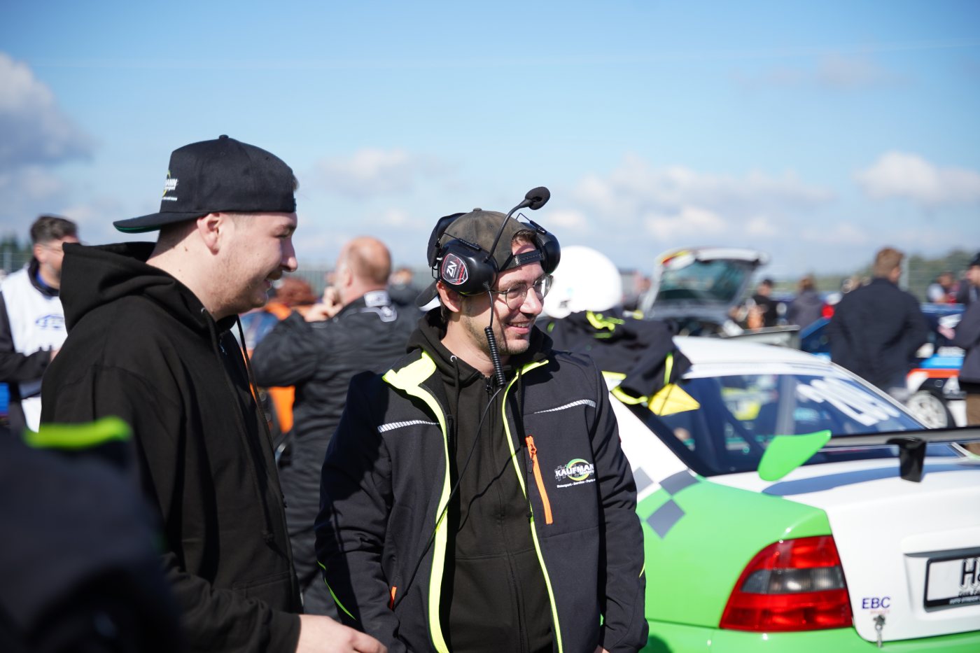 Zwei Mitarbeiter neben dem grün-weißen Vectra, einer davon mit Funk-Headset