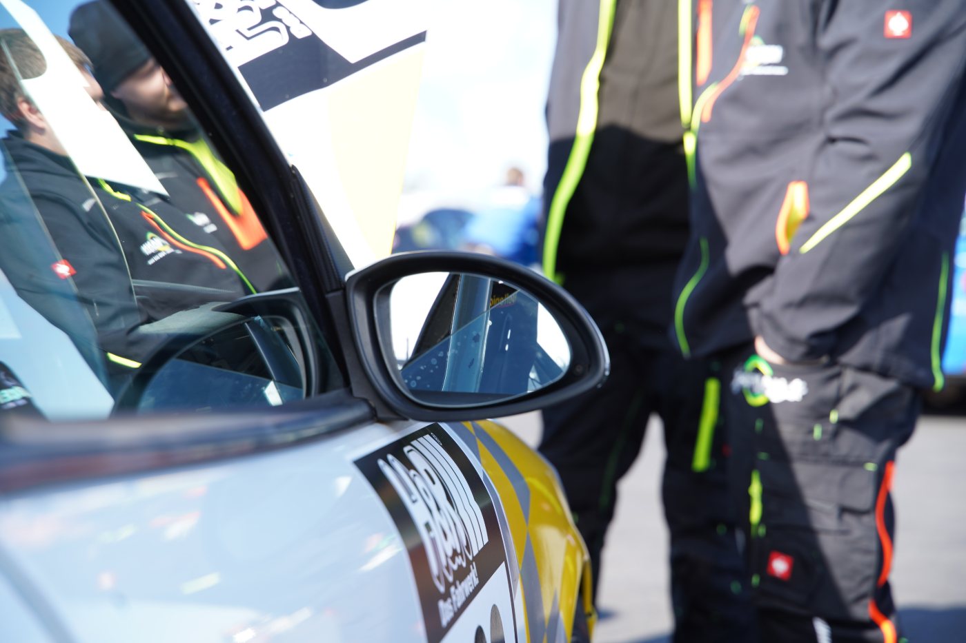 Nahaufnahme von Außenspiegel und Fahrertür des Vectra, daneben zwei Mitarbeiter in Kaufmann-Motorsport-Arbeitskleidung